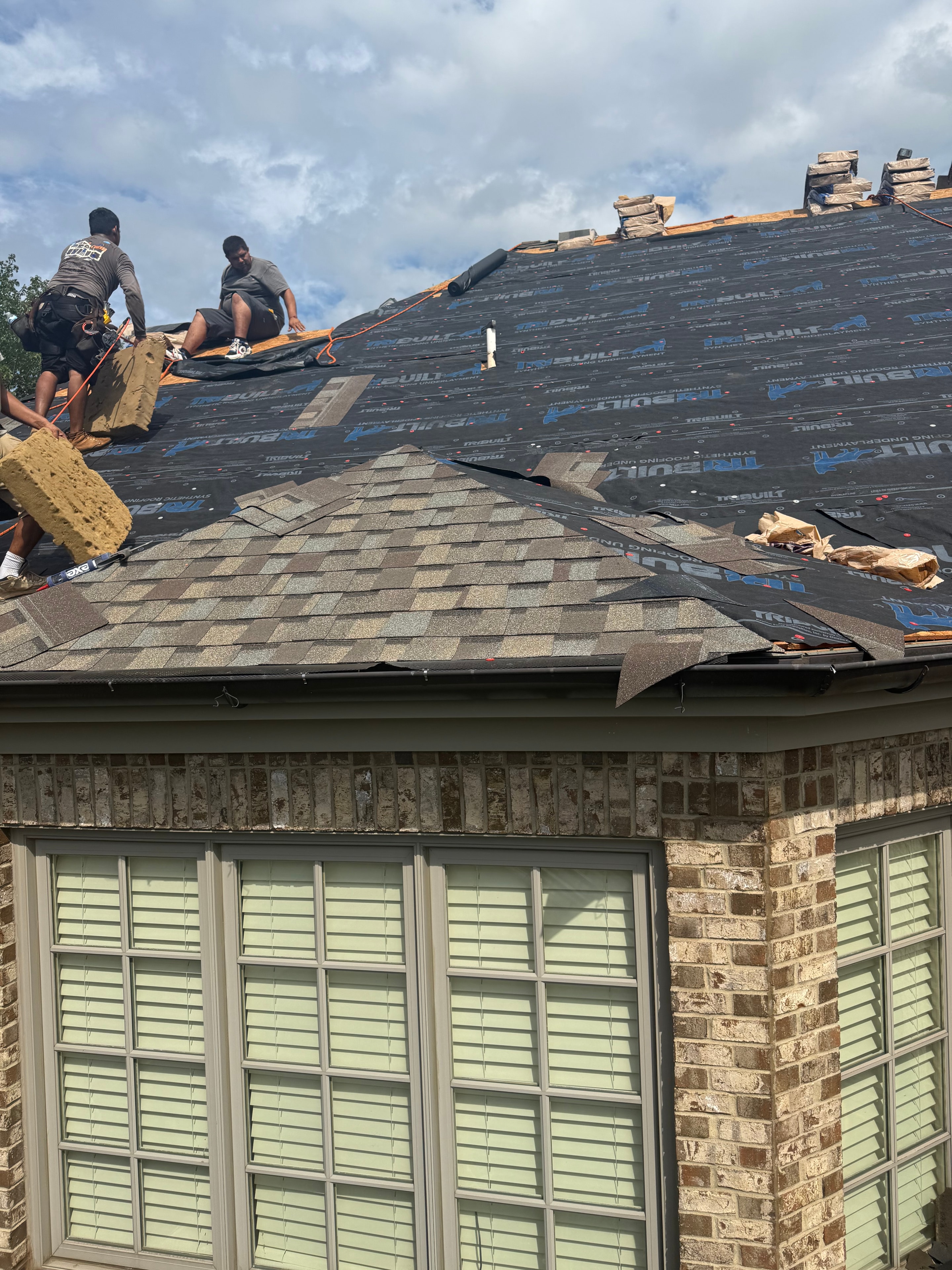 Crew installing shingles on large brick home