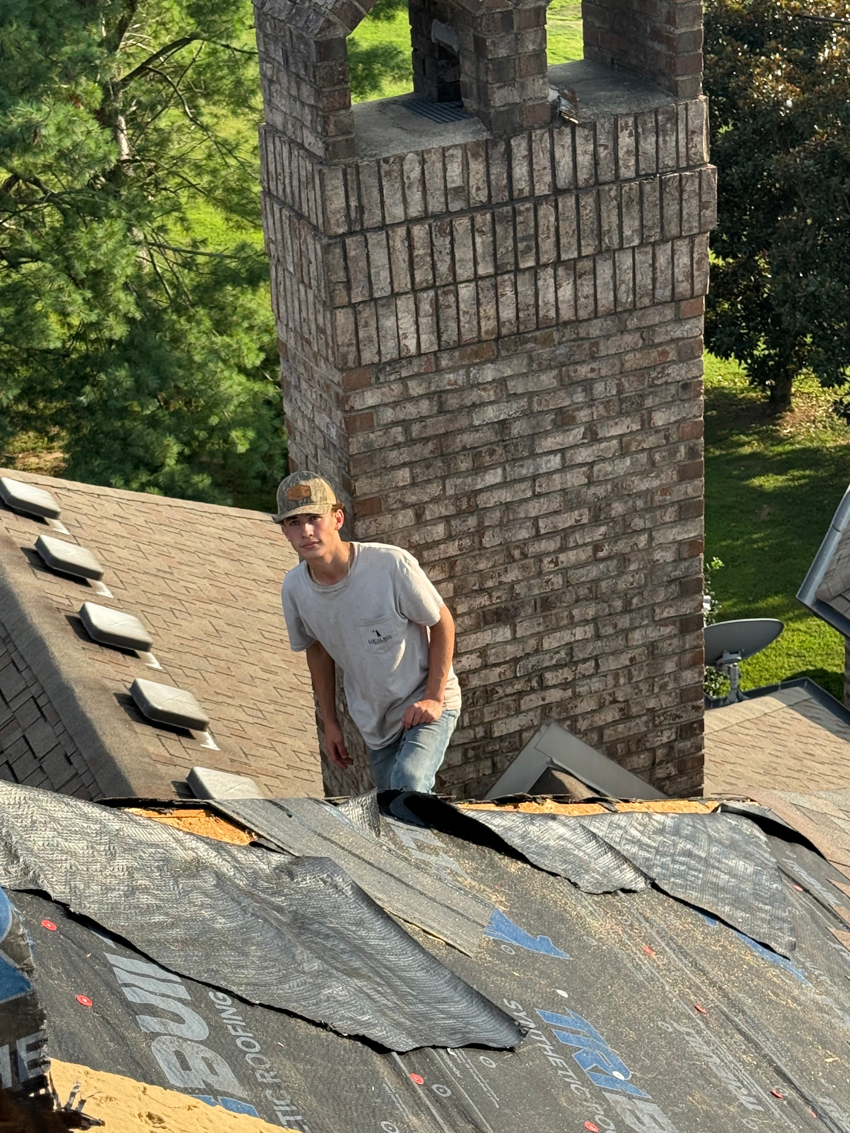 Roofer inspecting synthetic underlayment near chimney