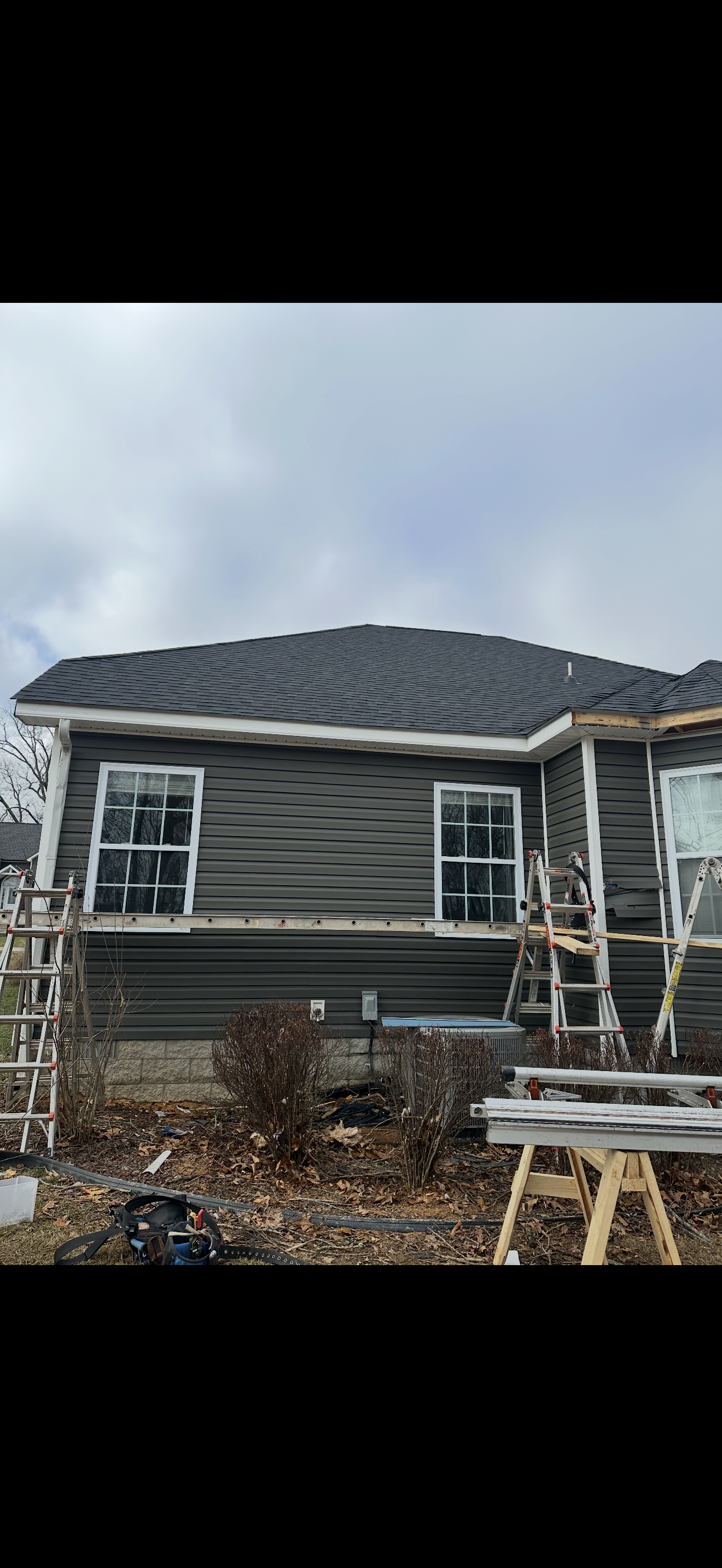 Completed dark shingle roof on gray siding home side view
