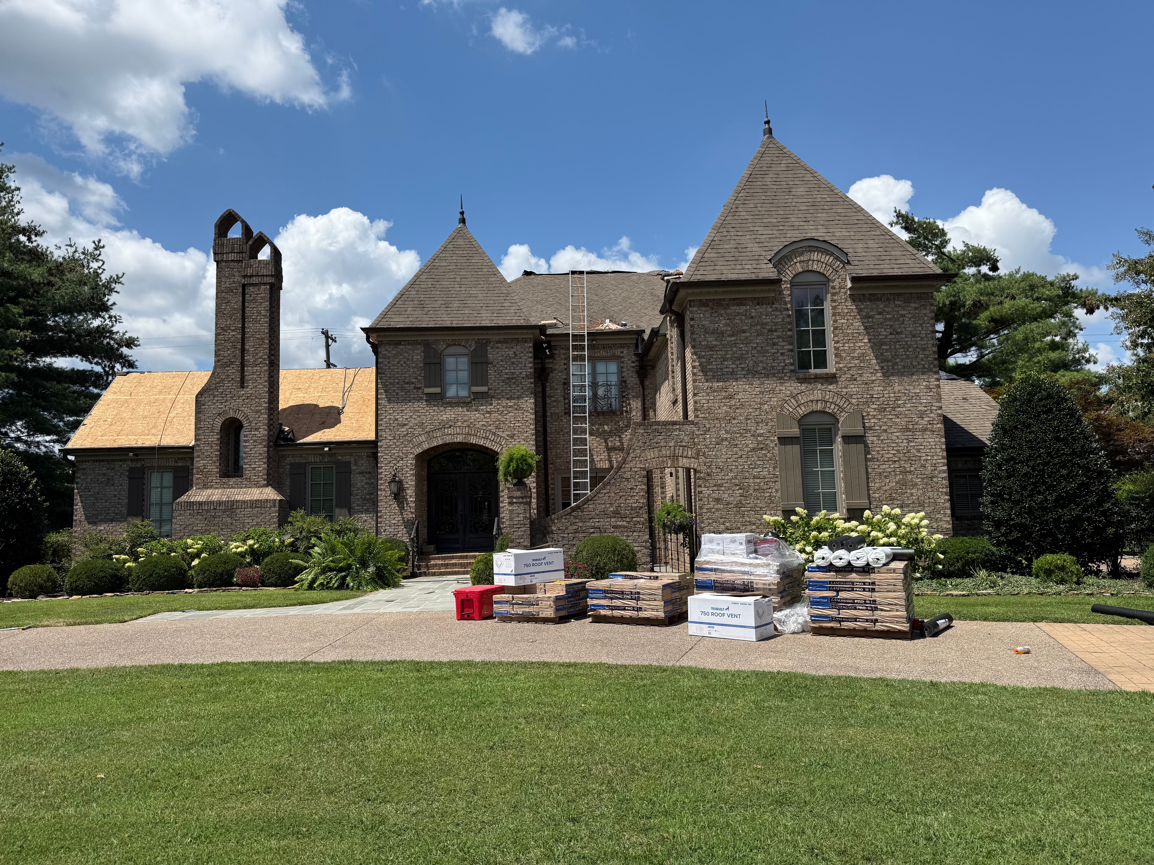 Large brick estate home mid roof replacement with materials staged on driveway