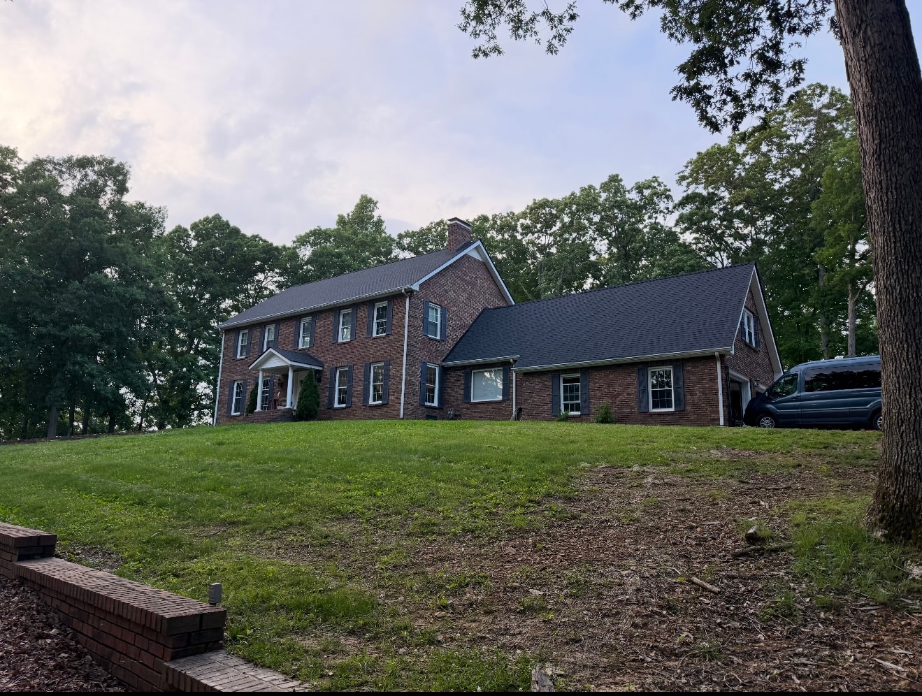 Completed dark shingle roof on brick colonial home on hillside