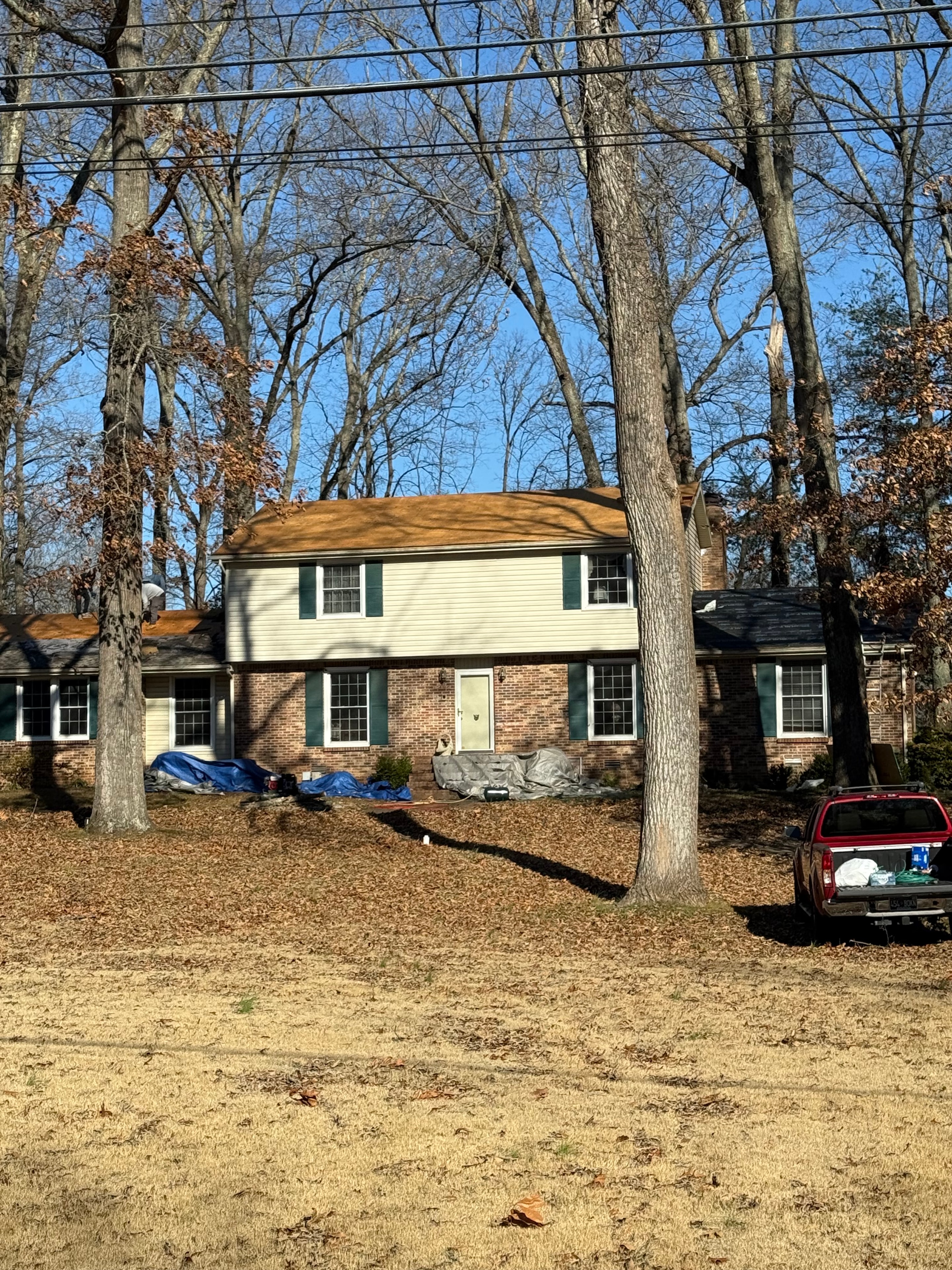 Storm-damaged home with large tree fallen on roof and blue tarps in place