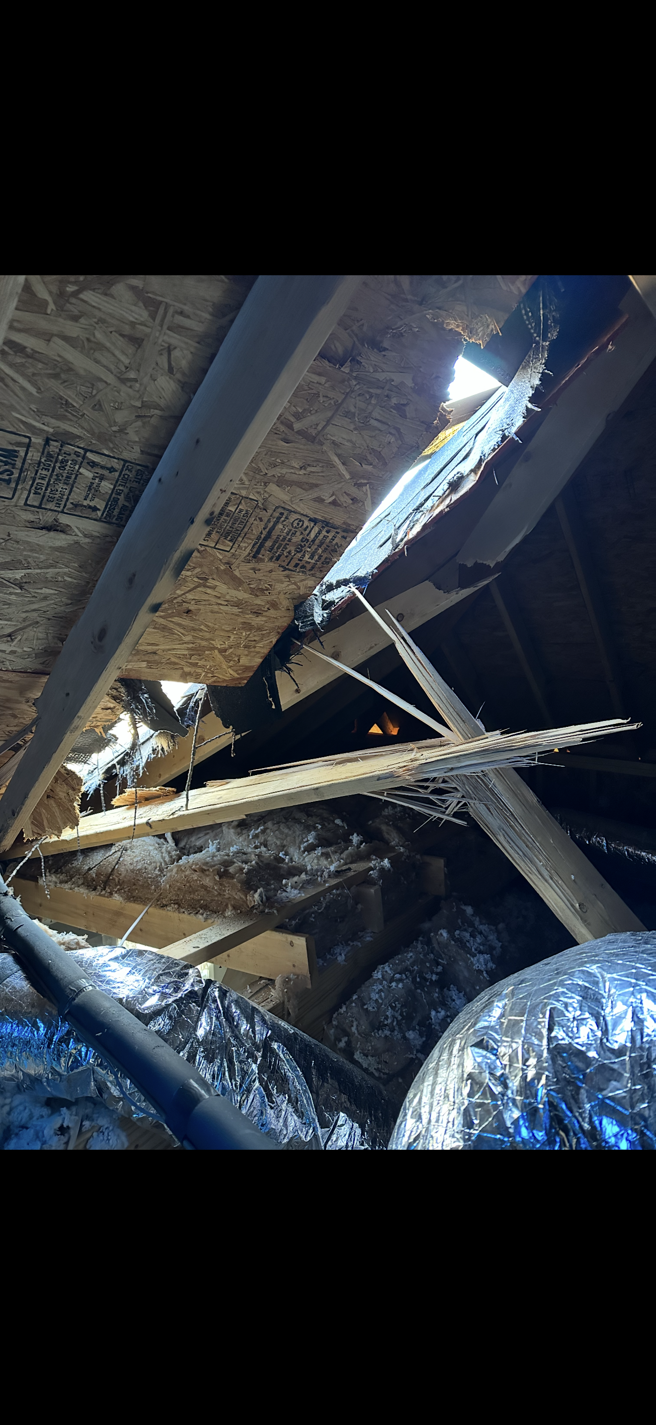 Interior attic view of storm-damaged roof with broken trusses and light coming through