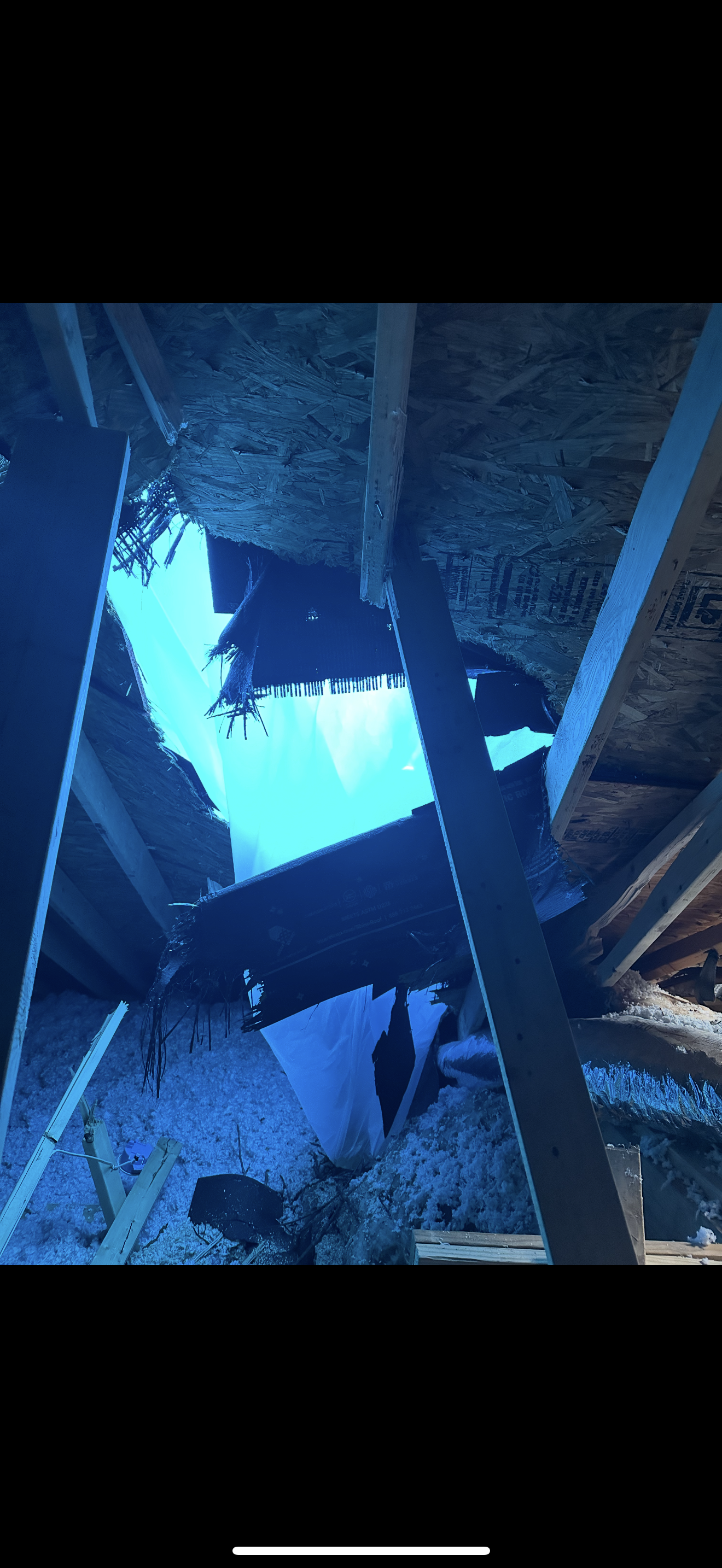 Interior attic view of collapsed roof decking with blue tarp visible through opening