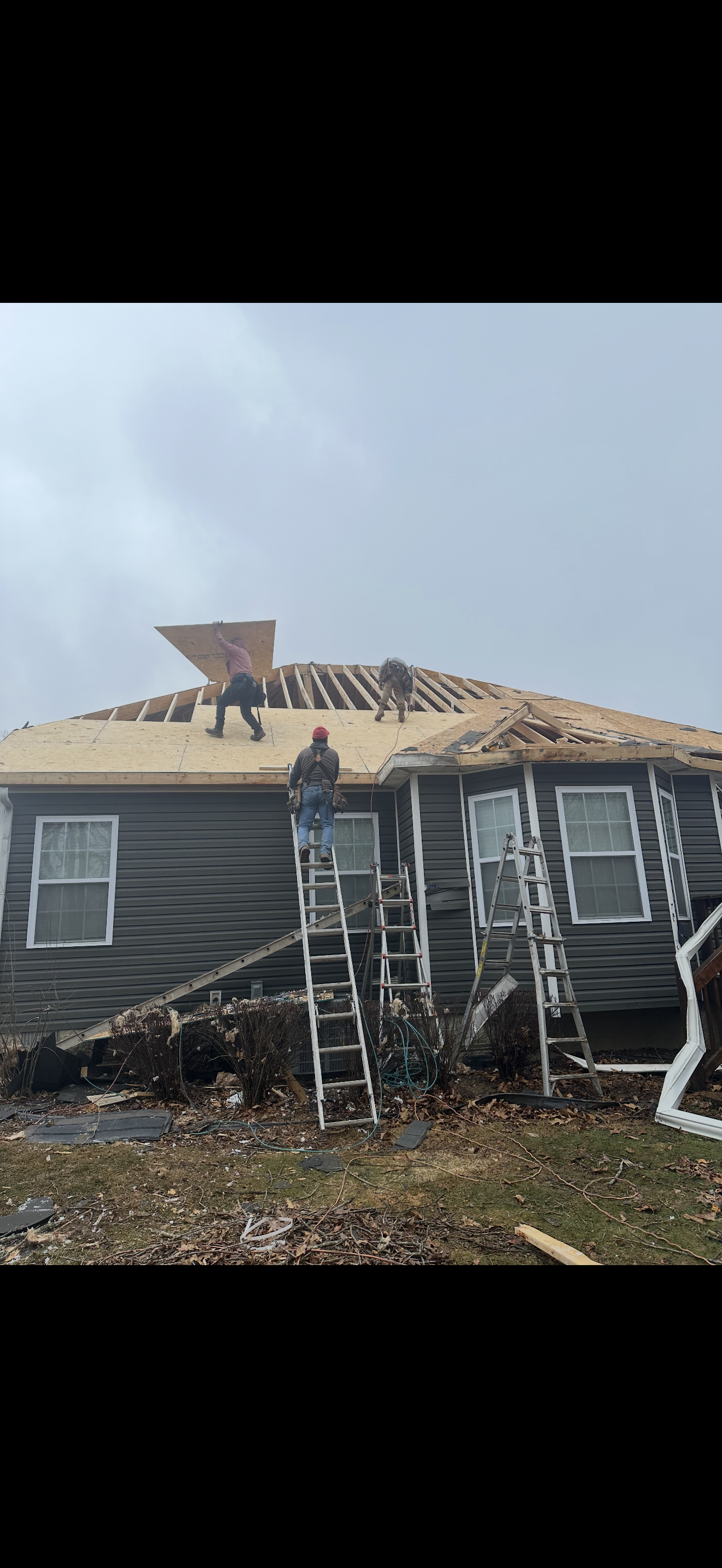 Three-man crew installing new OSB decking on gray home after storm damage