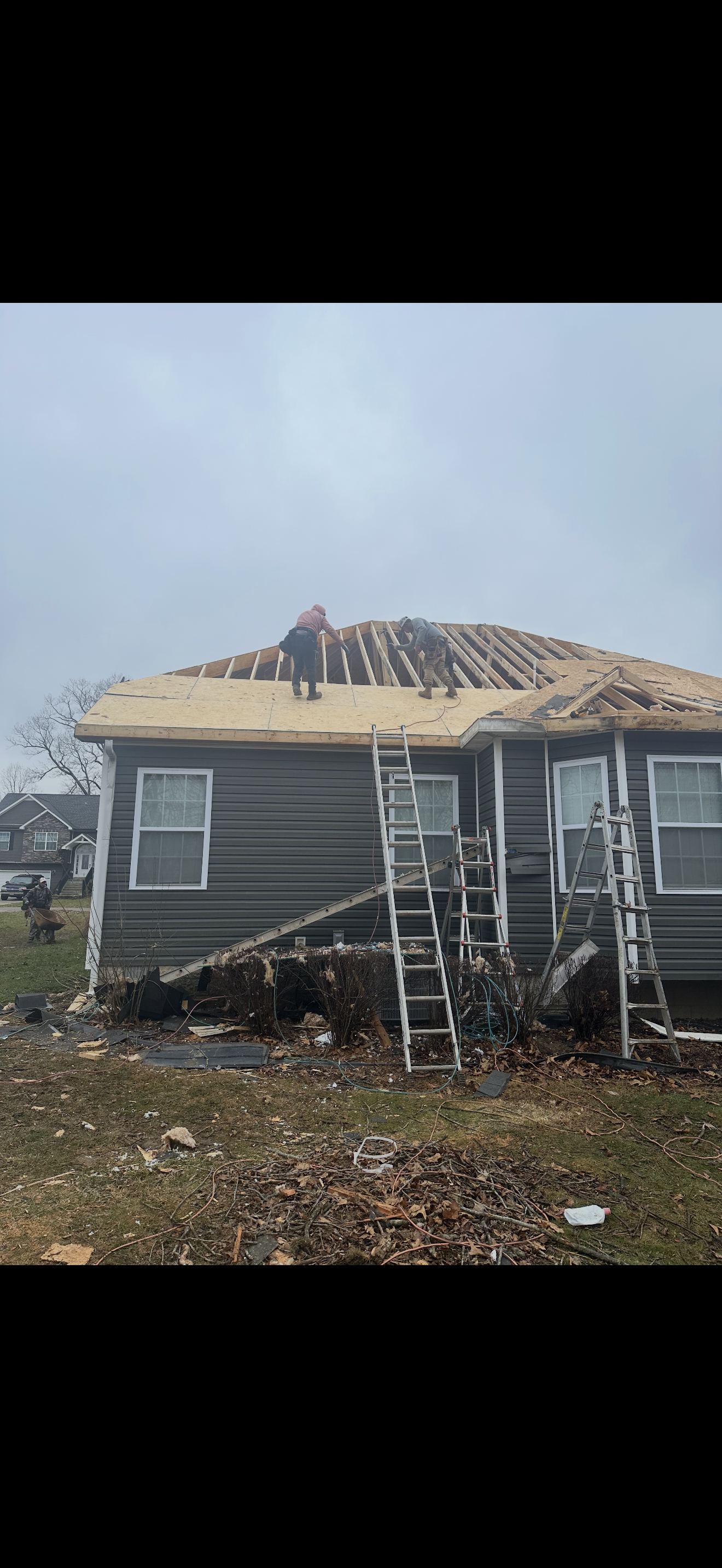 Crew replacing decking on gray home with exposed rafters and storm debris