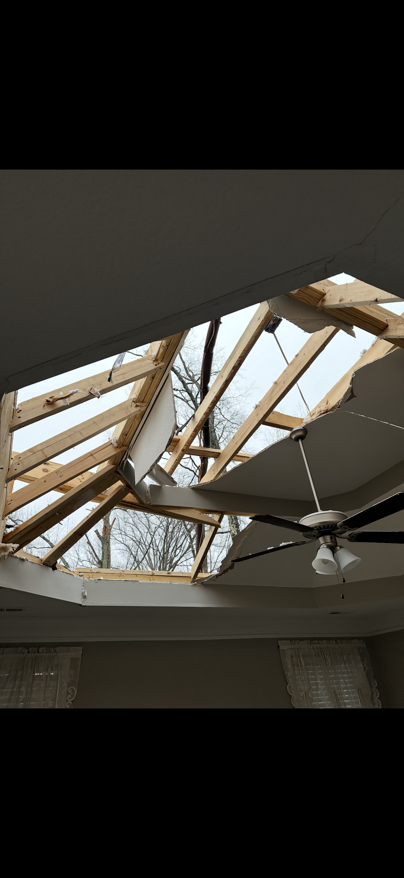 Interior view of storm-destroyed roof with ceiling fan and open sky visible