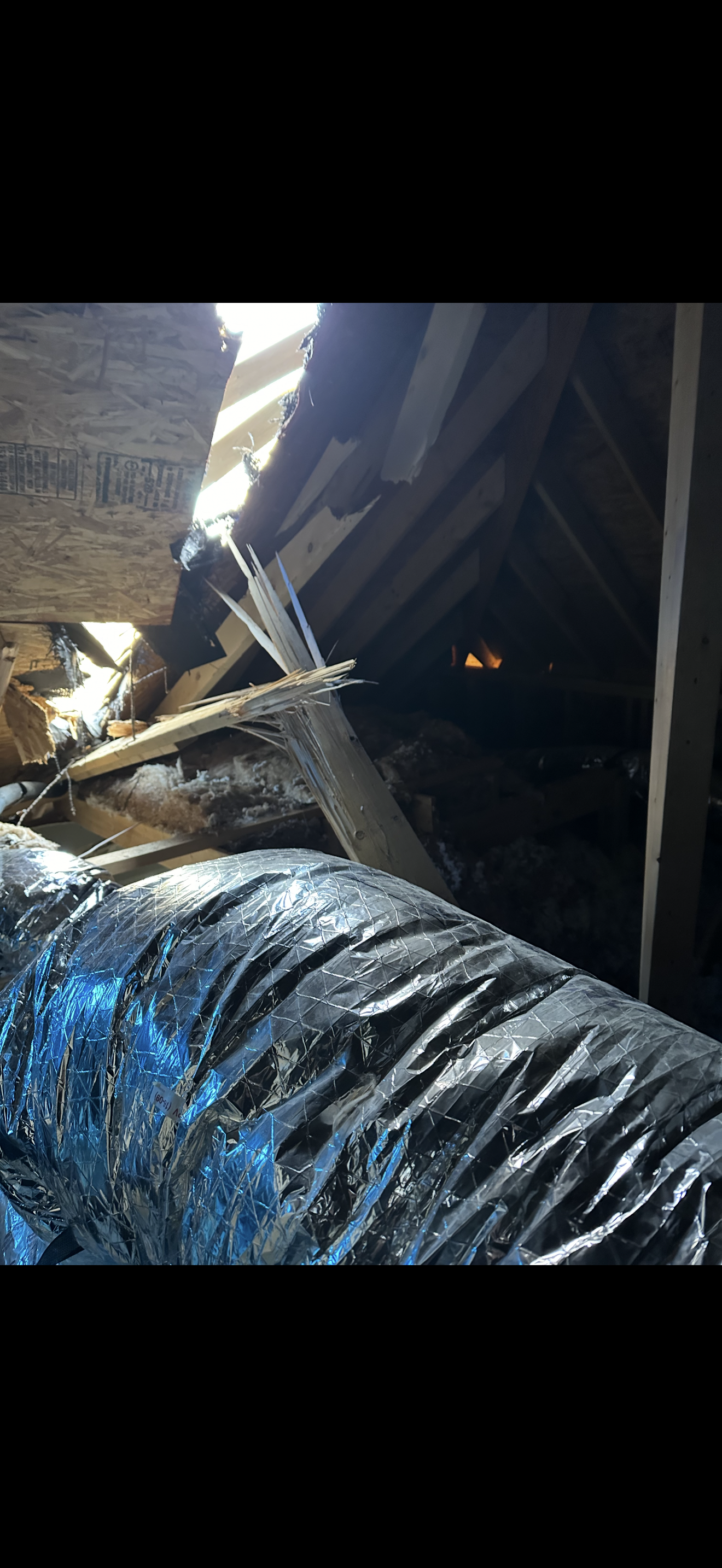 Attic view of storm-damaged roof with HVAC ductwork and broken rafters